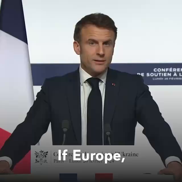 A video of Macron speaking at a lecture. There is a French flag immediately behind his right arm.