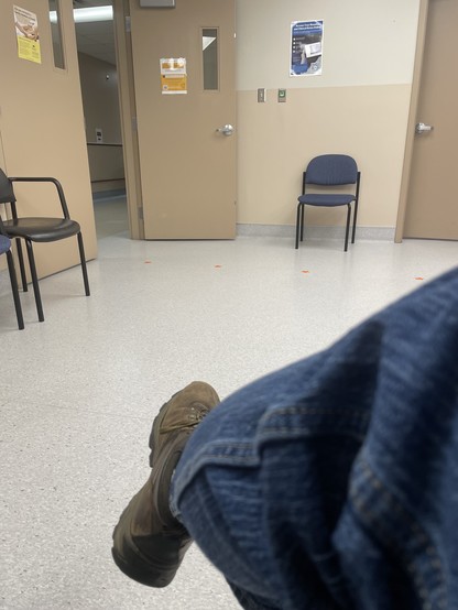 My crossed leg with booted foot as I sit in a sterile looking waiting room with two tone beige walls.