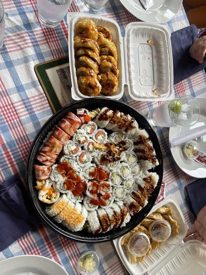 A large circular platter of various types of sushi sits on a table with a rectangular box of gyoza at the top
