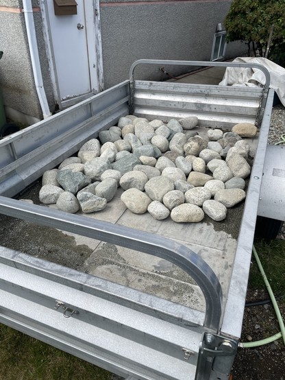 A silver trailer has its bed mostly covered in granite rocks of various sizes.