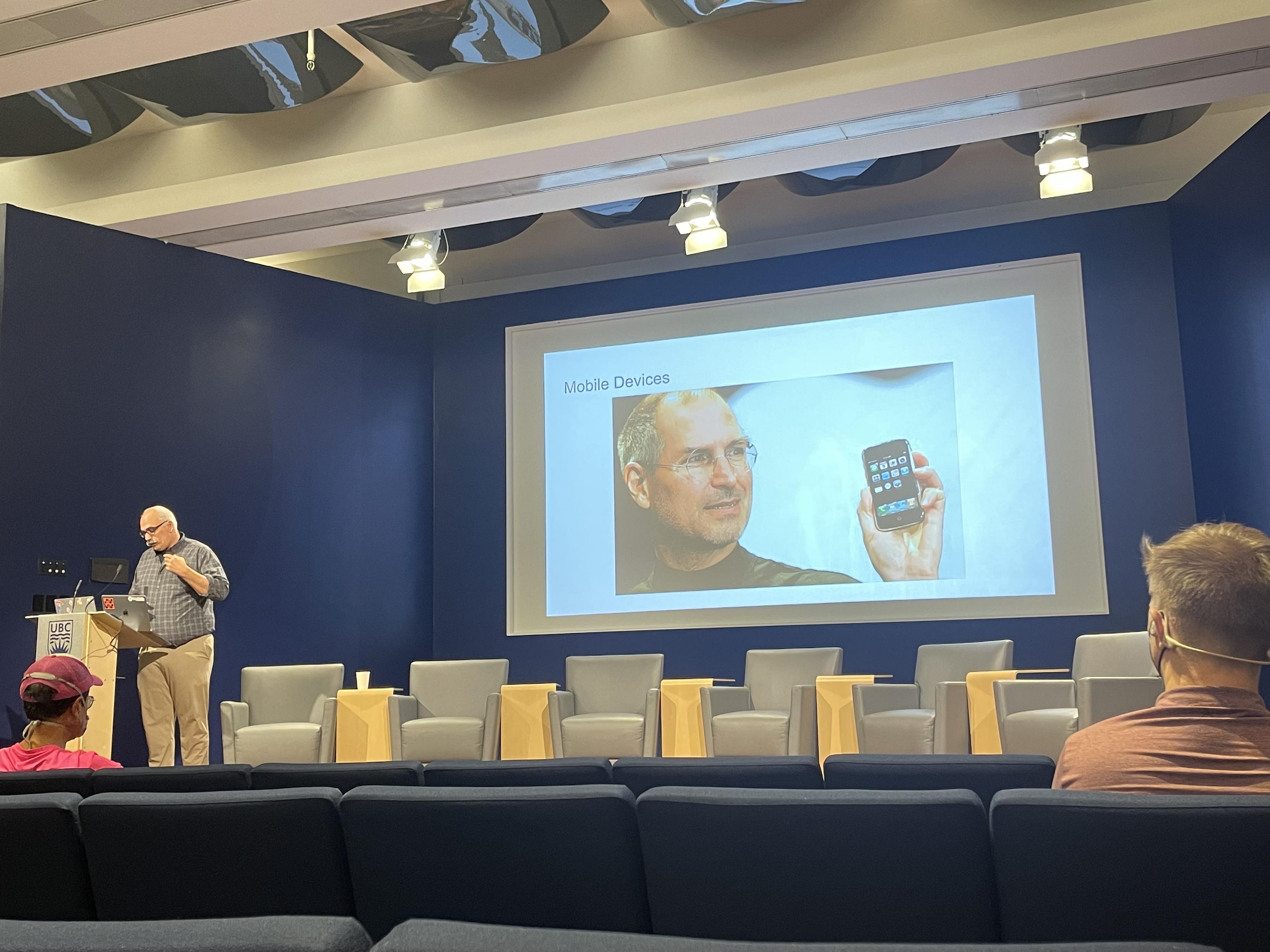 steve jobs on the screen with the first iphone aa evan speaks at a podium.