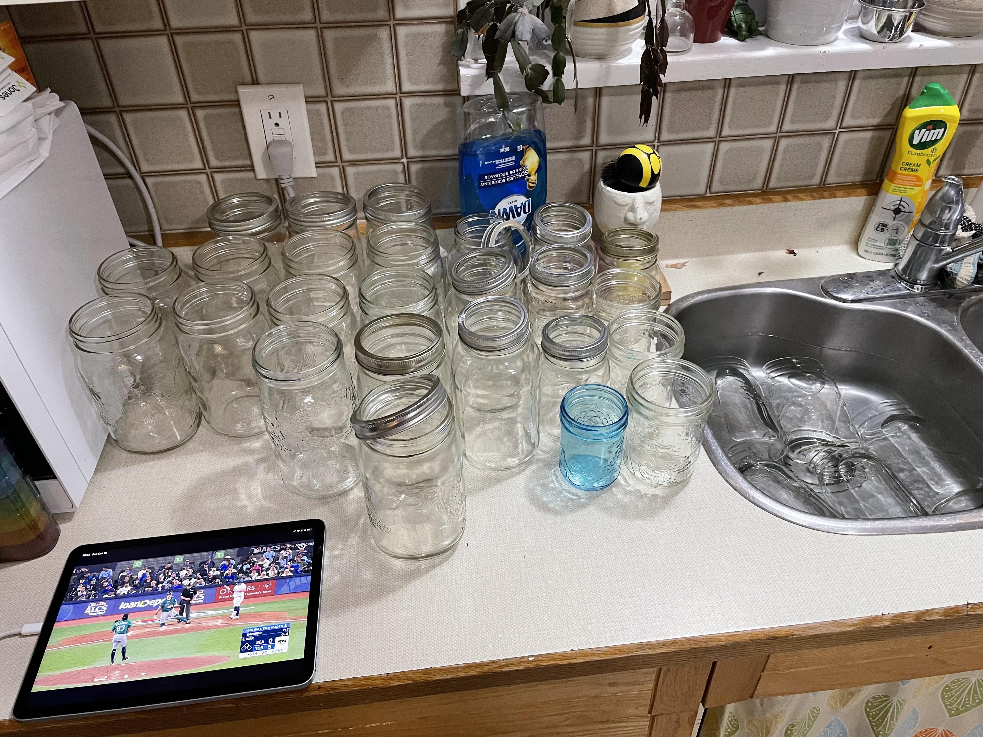 A group of clear glass wide mouse mason serves sits on a upright counter beside a silver still sink