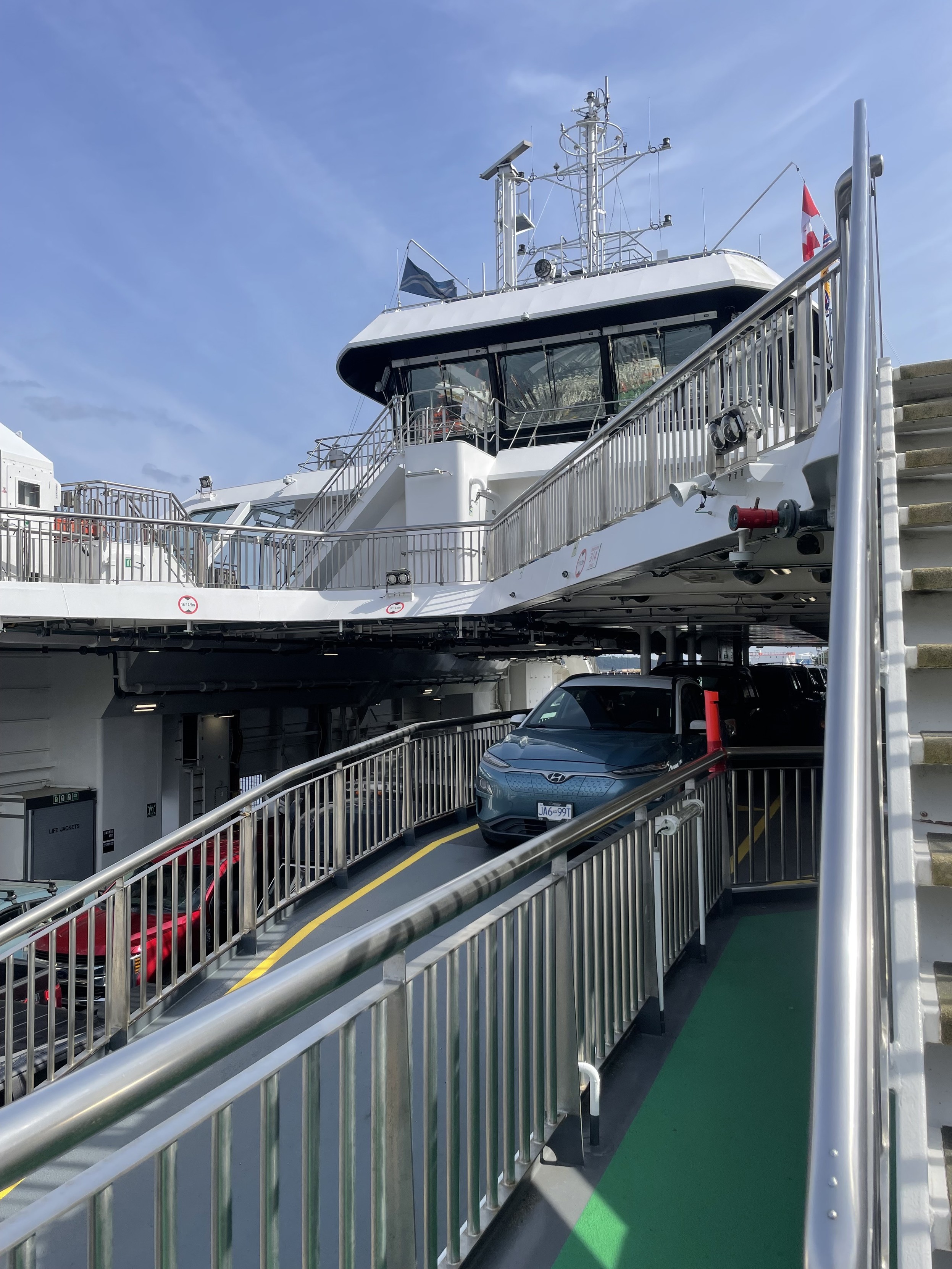 on the ferry looking back toward the car which is on a middle semi covered deck under the main bridge under blue sky