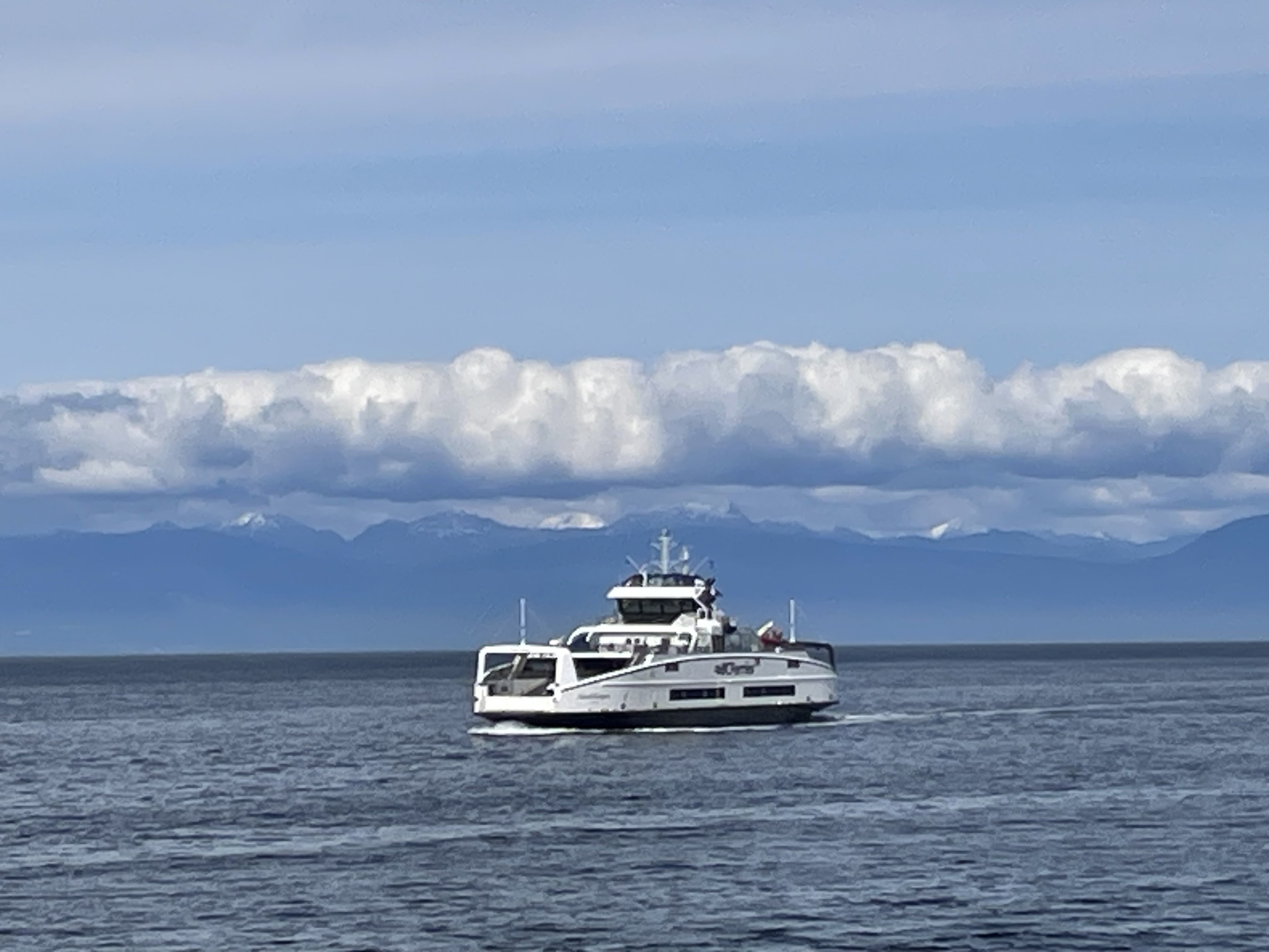 the ship against the far lower mainland shore, mountain range amd cloud deck and blue sky